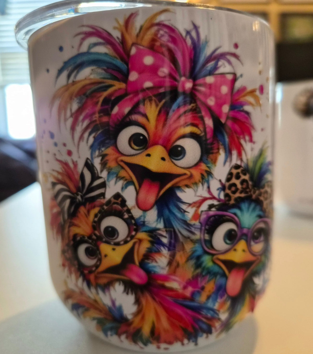 White tumbler featuring three colorful, wide-eyed cartoon birds with wild feathers, a pink polka-dot bow, and purple glasses.
