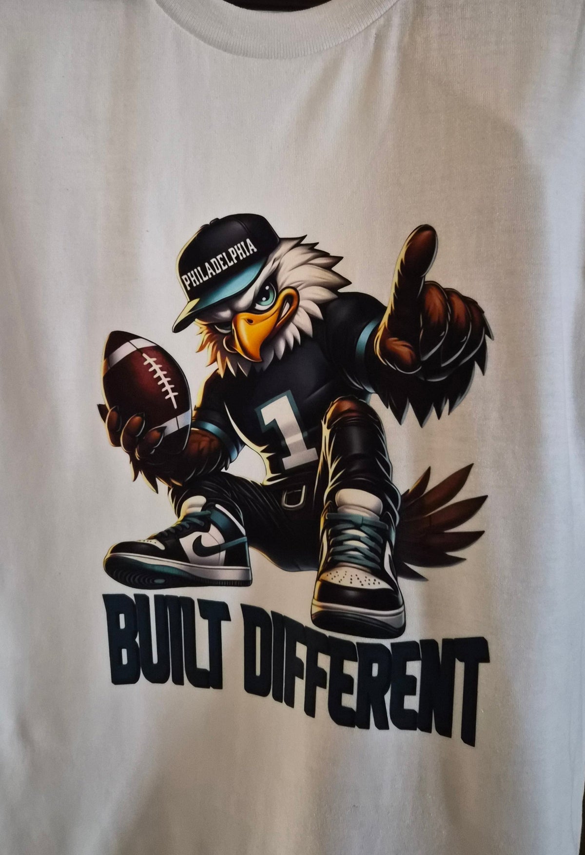 White graphic T-shirt with an eagle holding a football and Built Different text