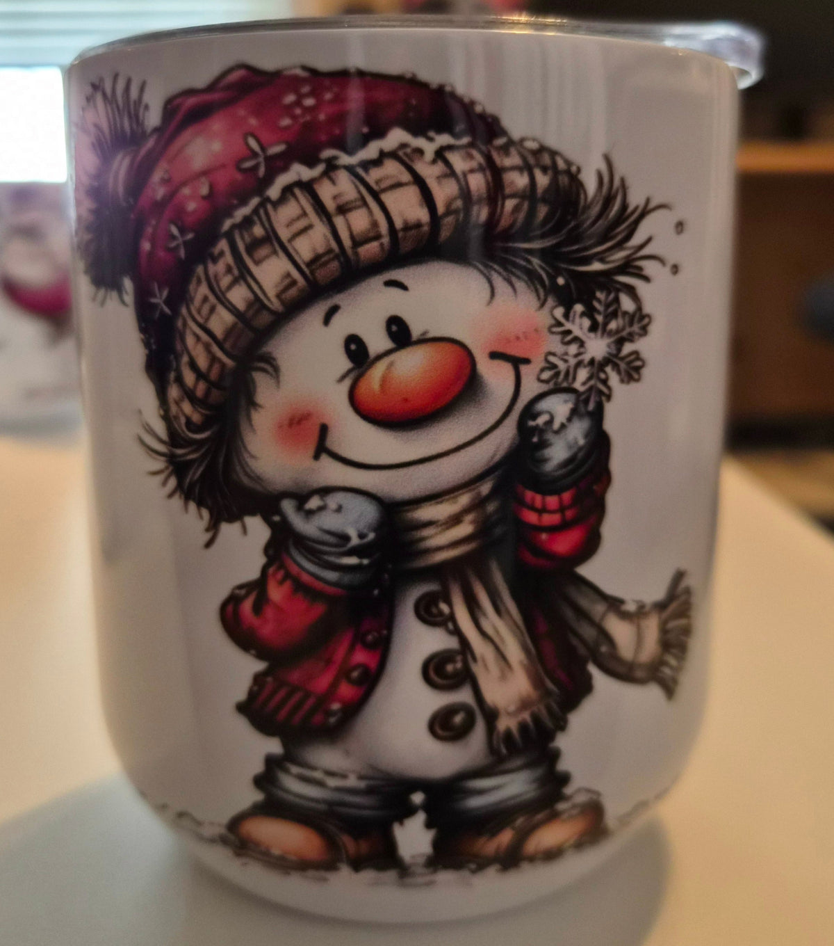 White tumbler featuring a smiling snowman with rosy cheeks, a red winter hat and mittens, a scarf, and a snowflake.